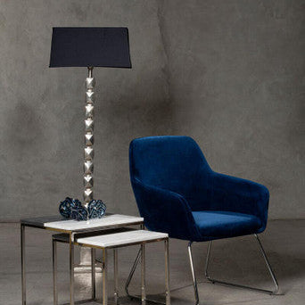 Blue armchair with nesting tables and a floor lamp against a gray wall.