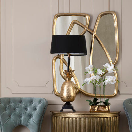 Decorative side table with gold lamp and mirror, flanked by two blue chairs against a beige wall.