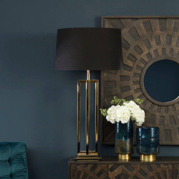 Decorative interior setting with a teal chair, lamp, and patterned cabinet against a dark wall.