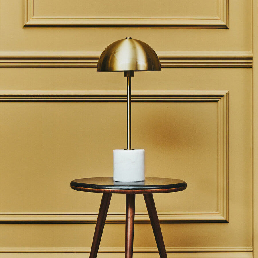 Gold table lamp on a wooden side table against a yellow paneled wall.