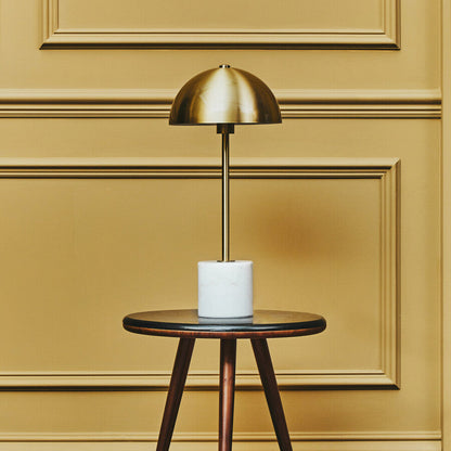 Gold table lamp on a wooden side table against a yellow paneled wall.