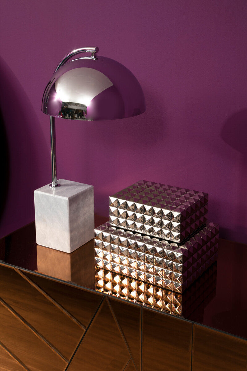 Silver lamp with a marble base on a reflective surface against a purple wall