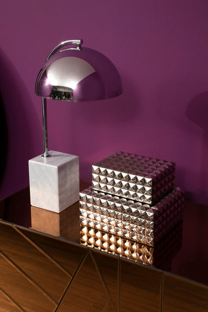 Silver lamp with a marble base on a reflective surface against a purple wall