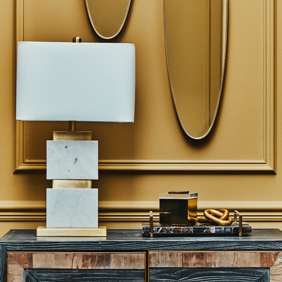 Decorative table lamp on a wooden console with gold wall art in the background