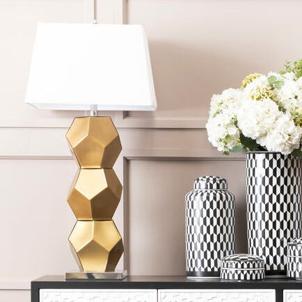 Decorative console table with lamps, vases, and a flower arrangement against a paneled wall.