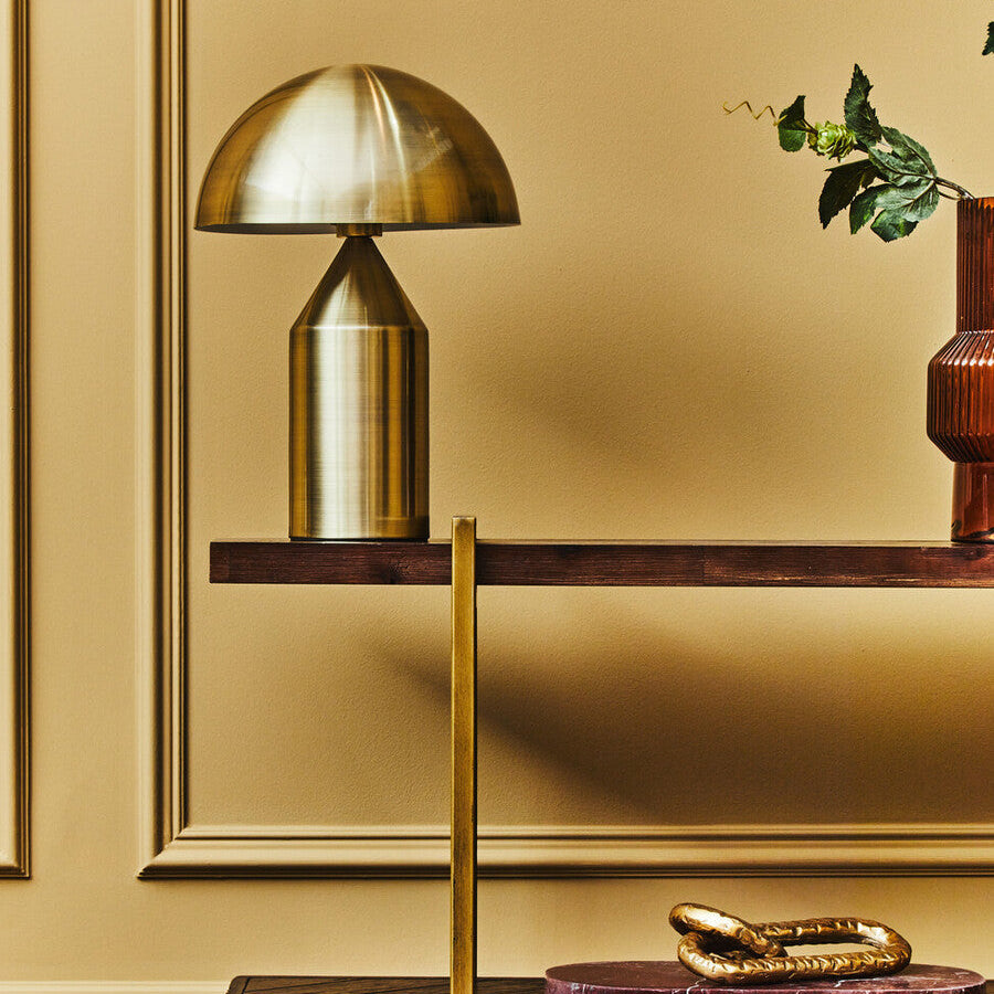 Gold table lamp on a wooden shelf against a gold wall