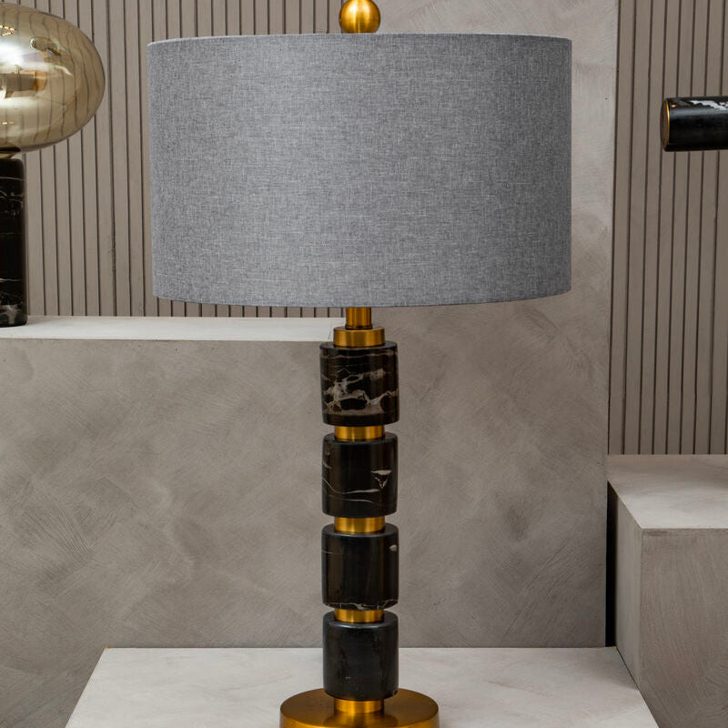 Table lamp with a gray shade, black and gold base on a white surface.