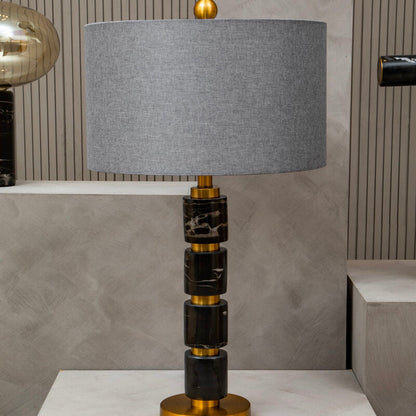 Table lamp with a gray shade, black and gold base on a white surface.
