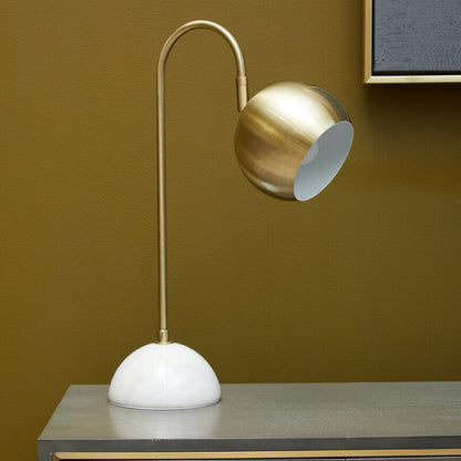 Modern table lamp with gold and white design on a wooden surface against a brown wall.