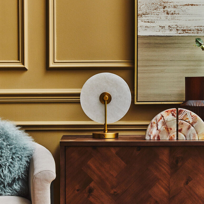 Decorative interior setting with a wooden cabinet, marble lamp, and abstract painting.