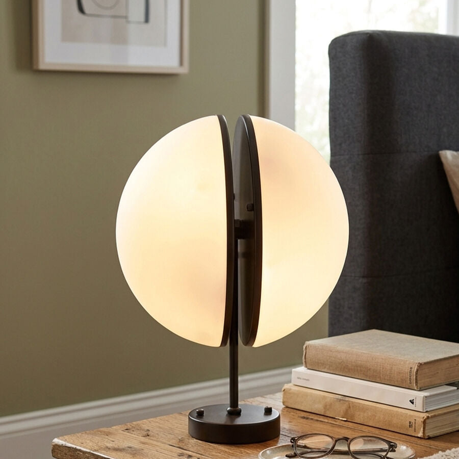 Table lamp on a wooden table with books and glasses in a cozy room setting.