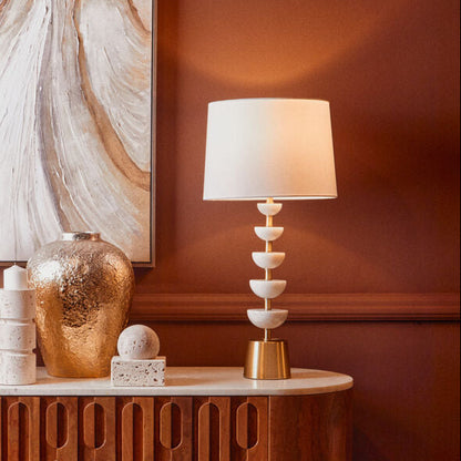 Decorative console table with a lamp and sculptures against a wall with abstract art.