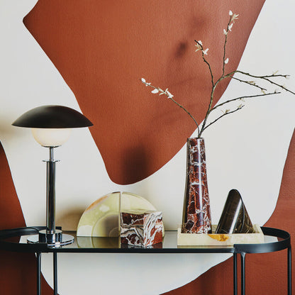 Modern interior design with a glass table, lamp, and decorative items against a wall with abstract brown and white shapes.