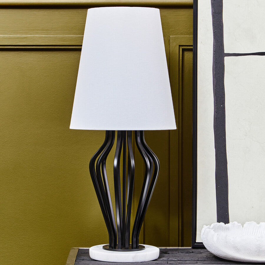 Table lamp with a white shade on a wooden surface against a green wall.