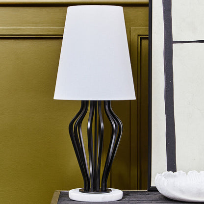 Table lamp with a white shade on a wooden surface against a green wall.
