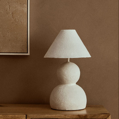 Beige table lamp on a wooden sideboard with a brown wall and abstract art in the background