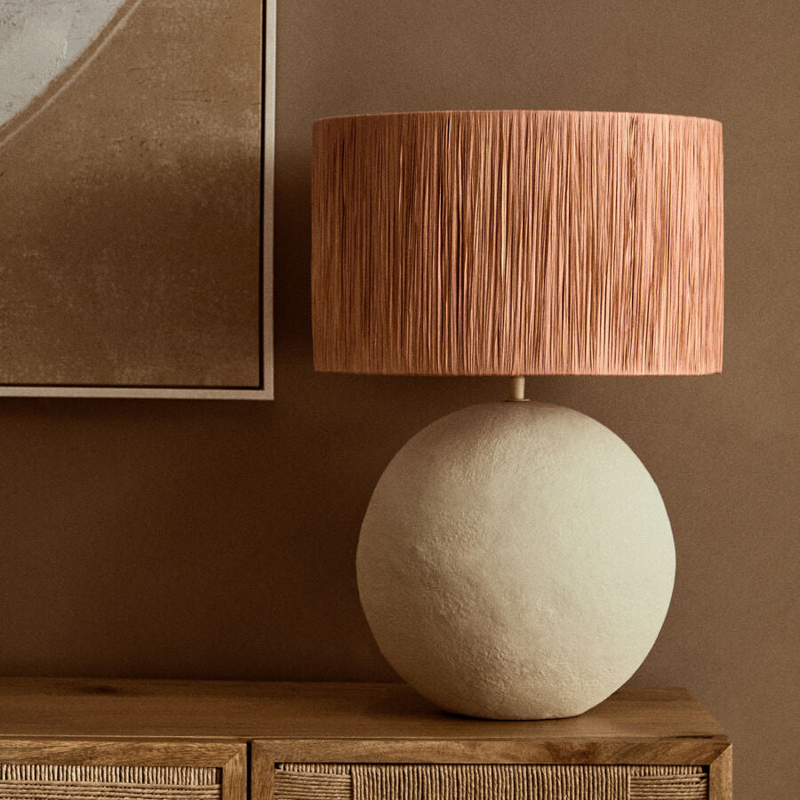 Table lamp with a textured brown shade on a wooden sideboard against a brown wall.