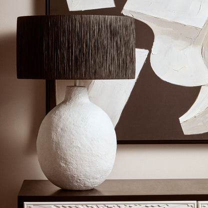 White textured vase with a black lampshade on a decorative cabinet against a wall with abstract art.