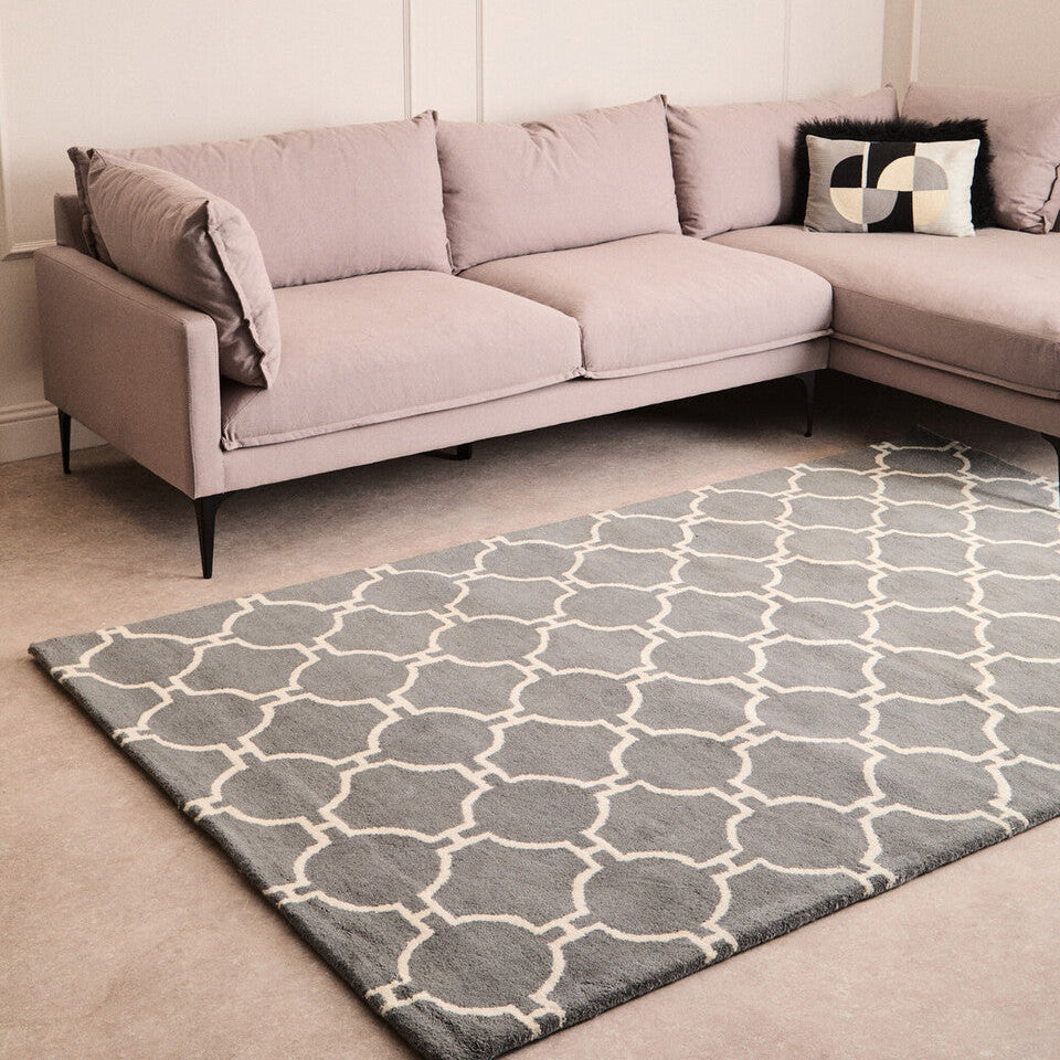 Gray patterned rug in front of a light gray sectional sofa with decorative pillows.