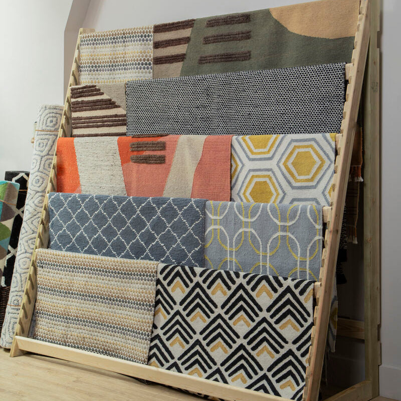 Wooden rack displaying various patterned rugs on a wooden floor.