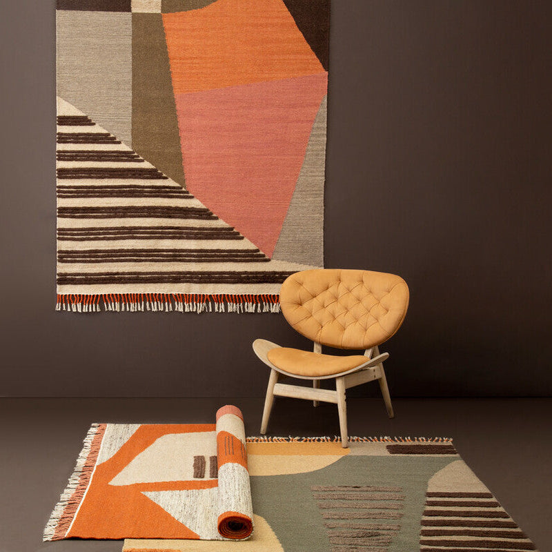 Rug with geometric pattern on a dark wall, chair, and another rug on a light surface.