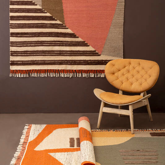 Rug with geometric pattern on a dark wall with a chair and rolled-up rug below.