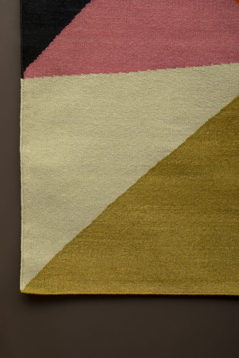 Colorful geometric-patterned rug with pink, beige, and green sections on a dark background