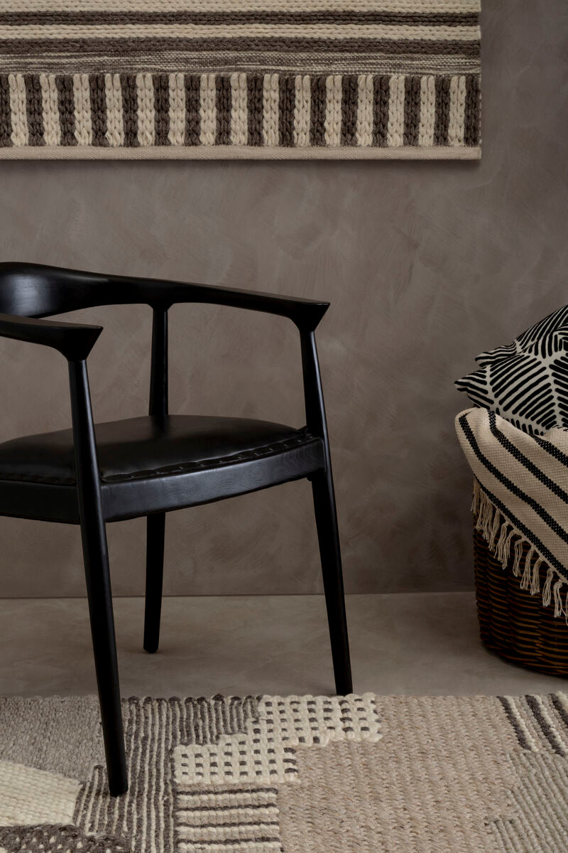 Black chair and woven basket against a textured wall with a rug on the floor.
