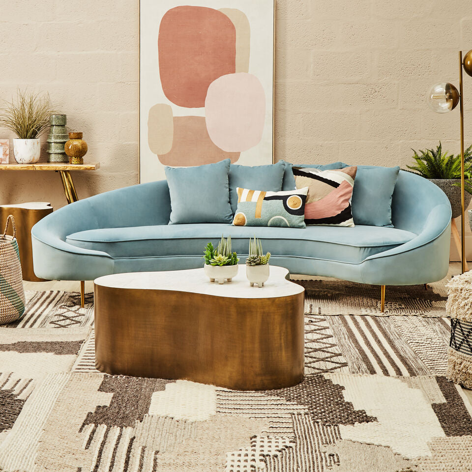 Modern living room with a curved light blue sofa, abstract art, and decorative items.