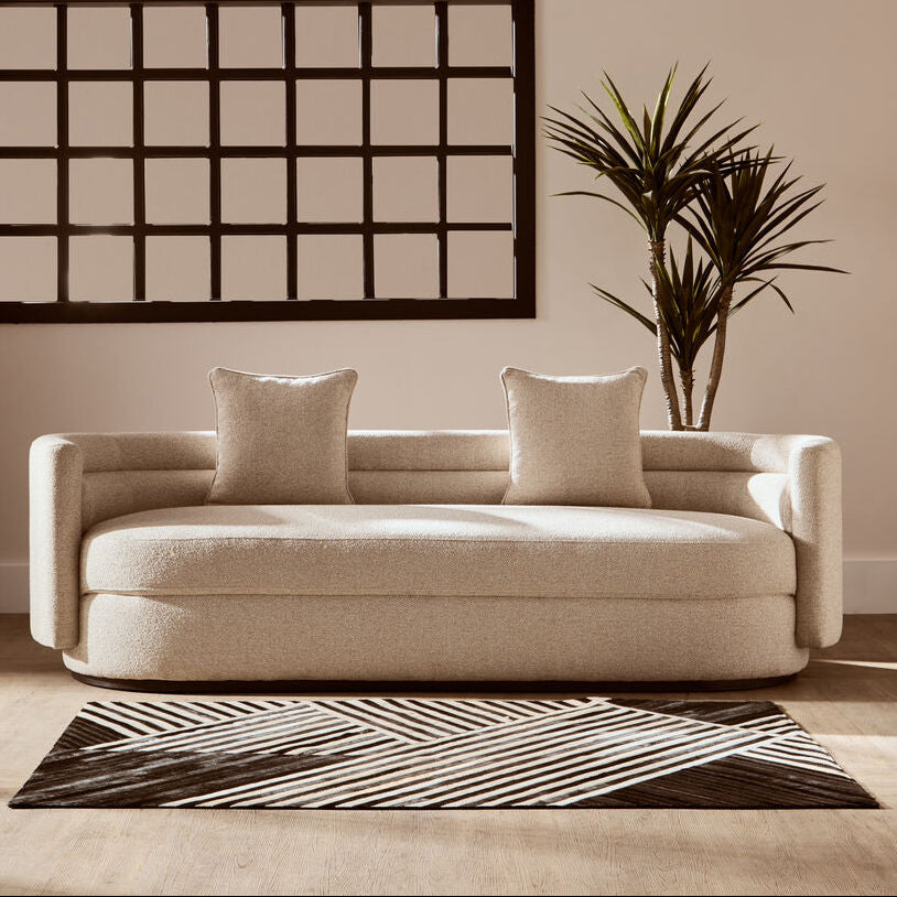 Beige sofa with two cushions in a room with a wall art piece and plant.