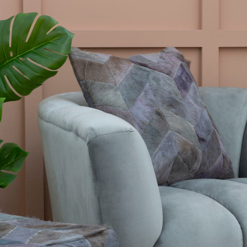 Light gray armchair with a patterned pillow against a beige wall.