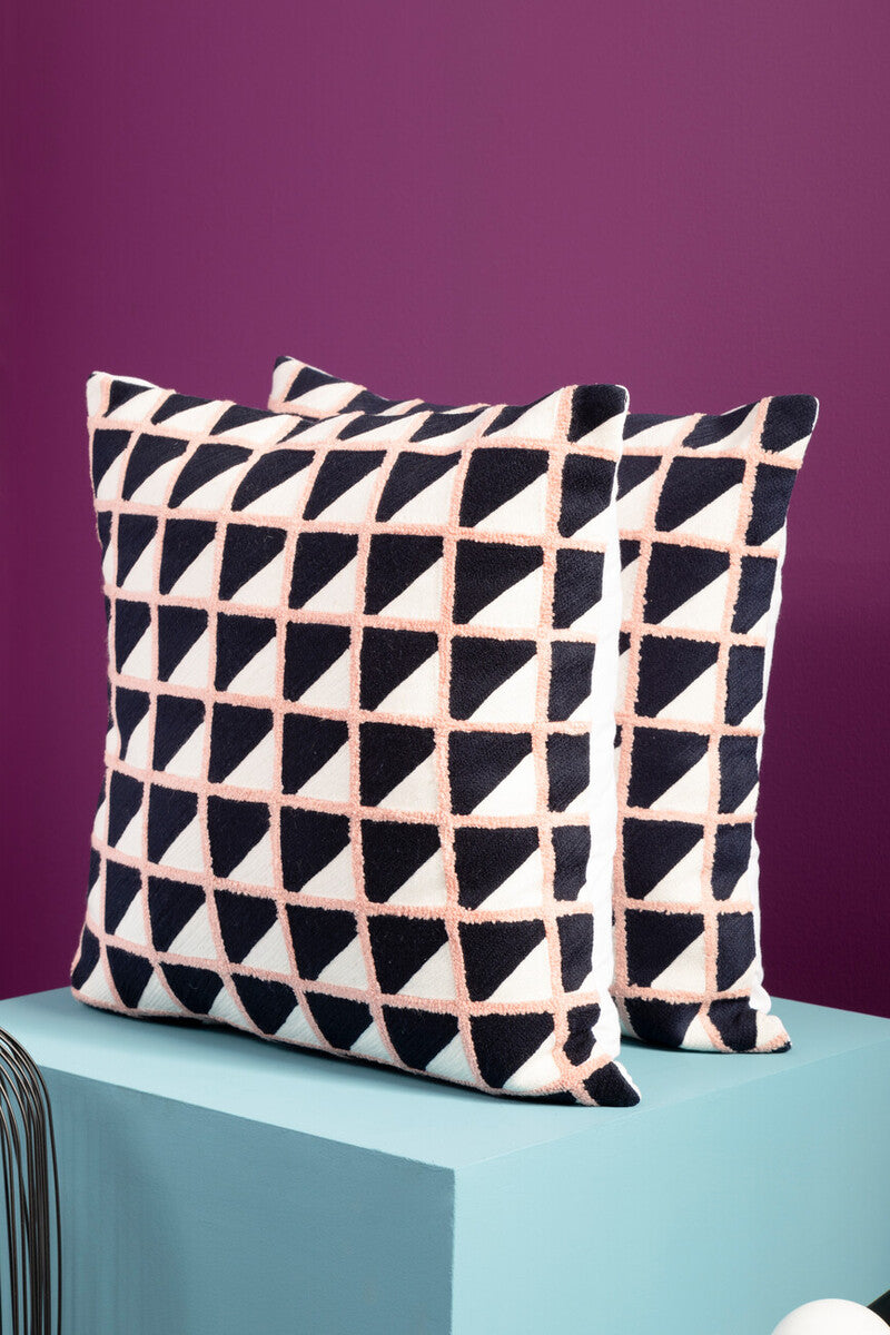 Two geometric-patterned pillows on a teal surface with a purple background