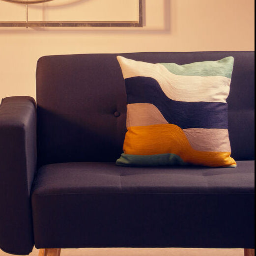 Modern living room with a dark purple sofa, small round table with a plant, and textured stool.
