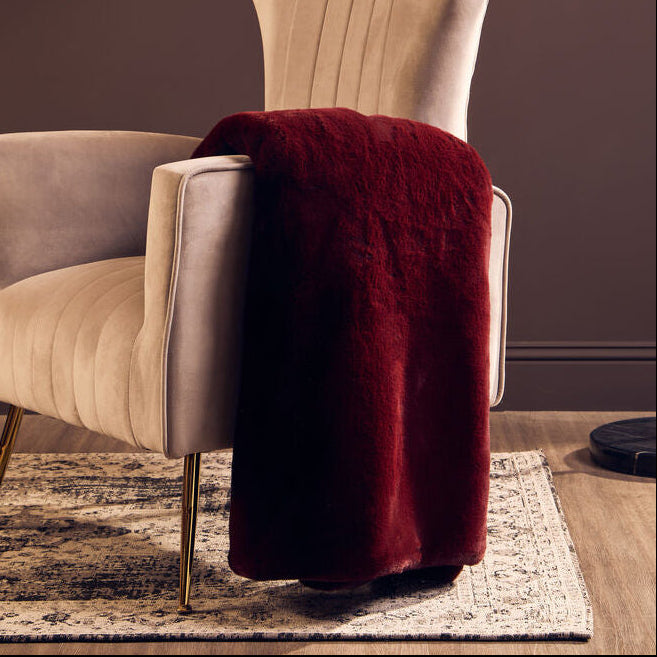 Beige armchair with a red blanket and a tall floor lamp against a dark wall.