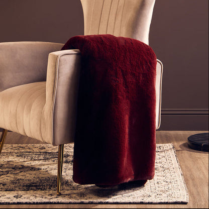 Beige armchair with a red blanket and a tall floor lamp against a dark wall.