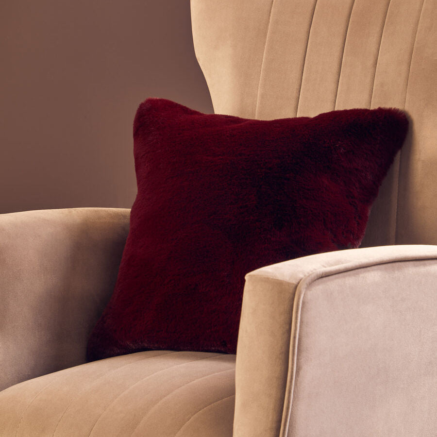 Beige armchair with a burgundy pillow against a brown background