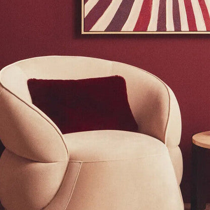 Modern beige armchair with a red pillow in a room with a red wall and a framed artwork.