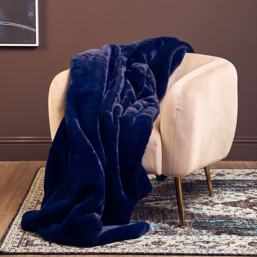Navy blue blanket draped over a beige armchair against a brown wall.
