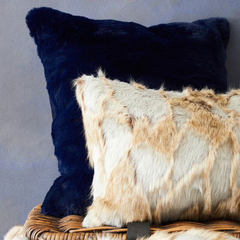 Two pillows, one navy and one with a fur pattern, on a textured surface.