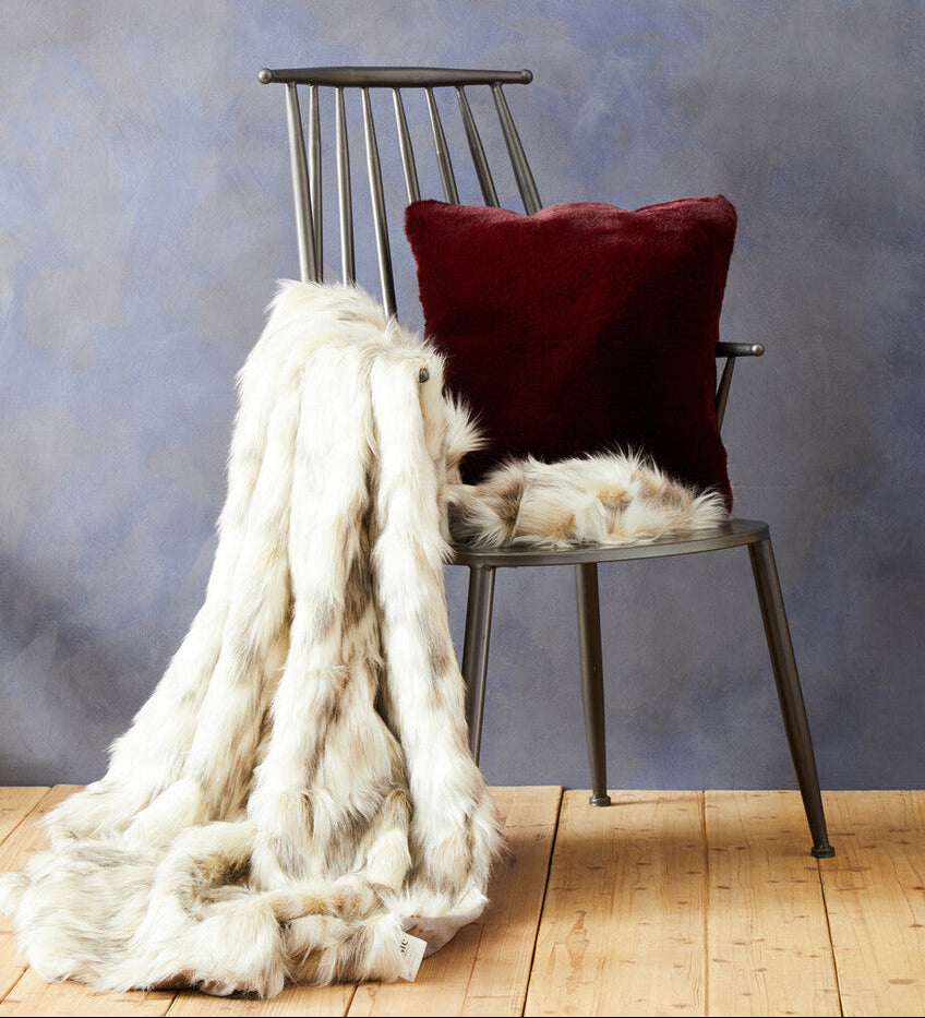 Chair with a red pillow and white fur throw against a textured blue wall.