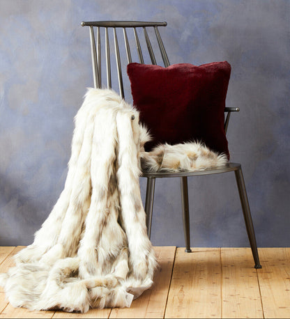Chair with a red pillow and white fur throw against a textured blue wall.