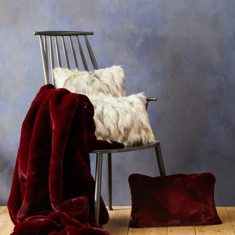 Chair with white fur pillow and red blanket against a textured blue wall