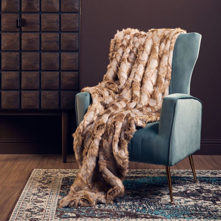 Blue armchair with a fur throw blanket in a room with a dark brown wall and wooden floor.