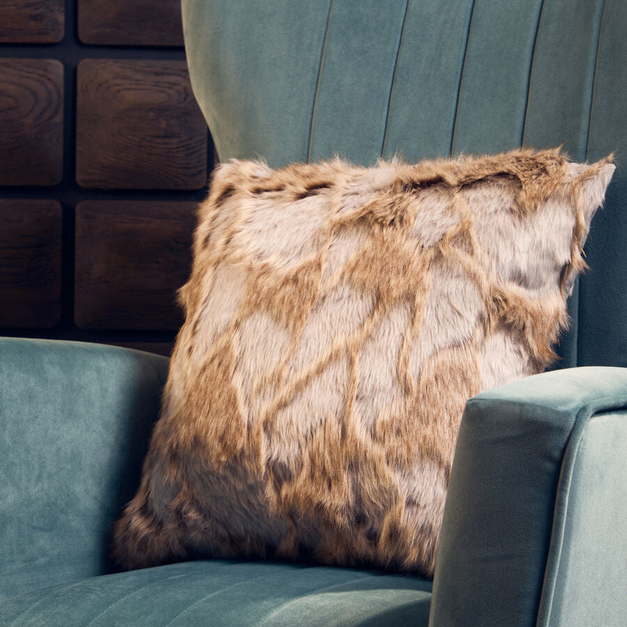 Fur pillow on a teal sofa against a wooden paneled wall