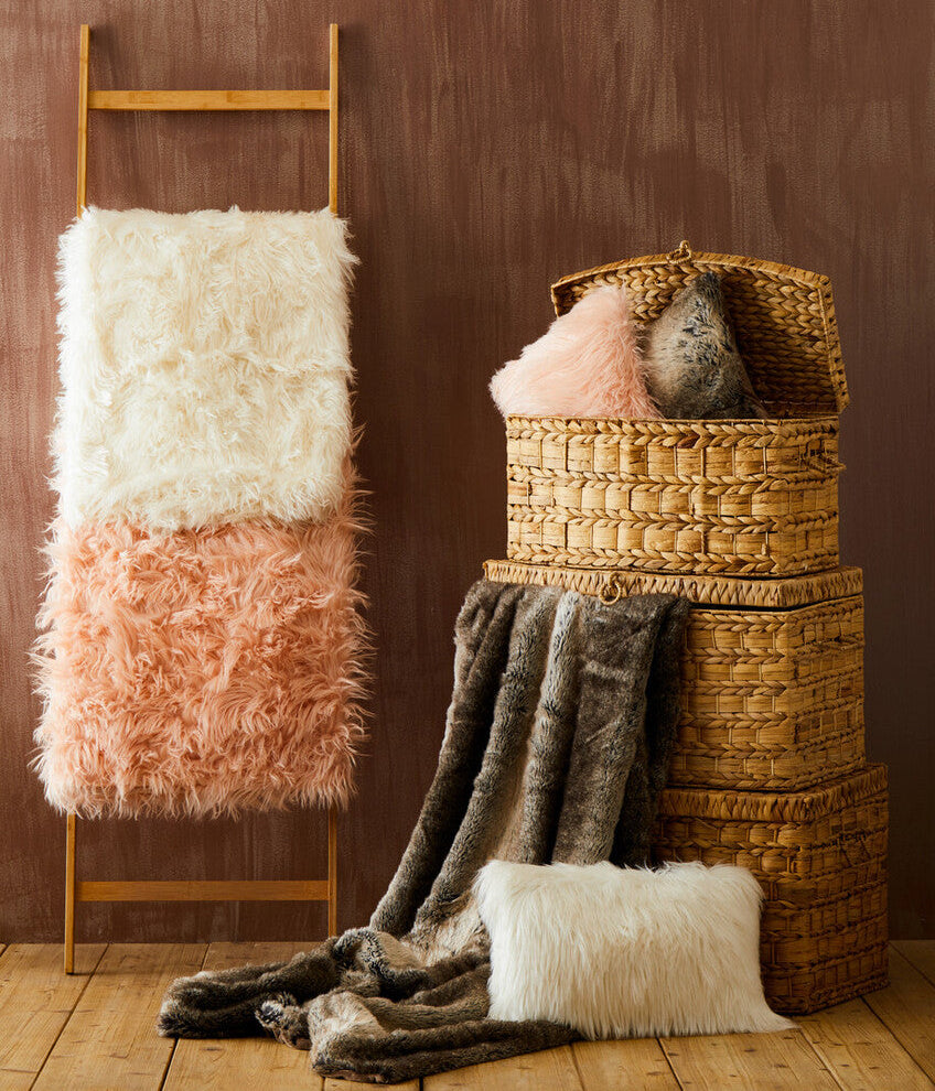 Fluffy blanket on a wooden ladder against a brown wall with wicker baskets and more blankets.