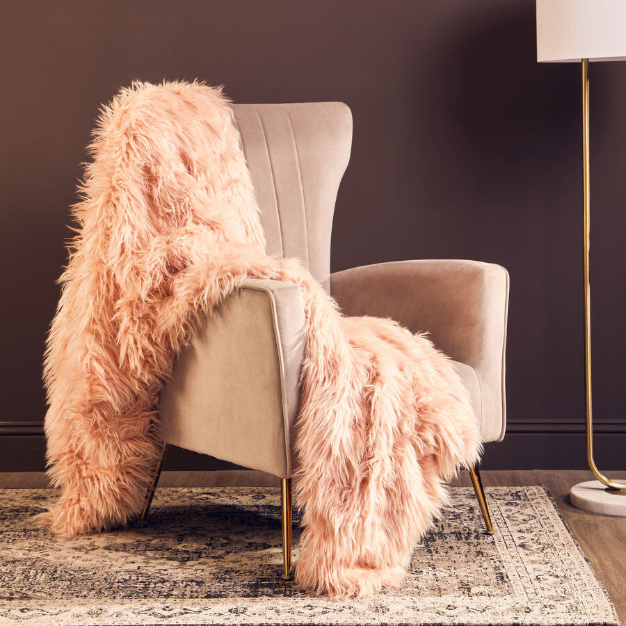 Beige armchair with a pink fur throw blanket in a room with a dark wall and floor lamp.
