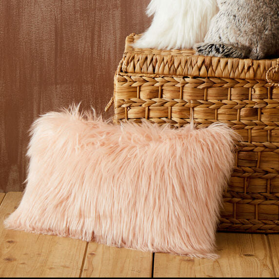 Wicker basket with fluffy pillows against a wooden wall