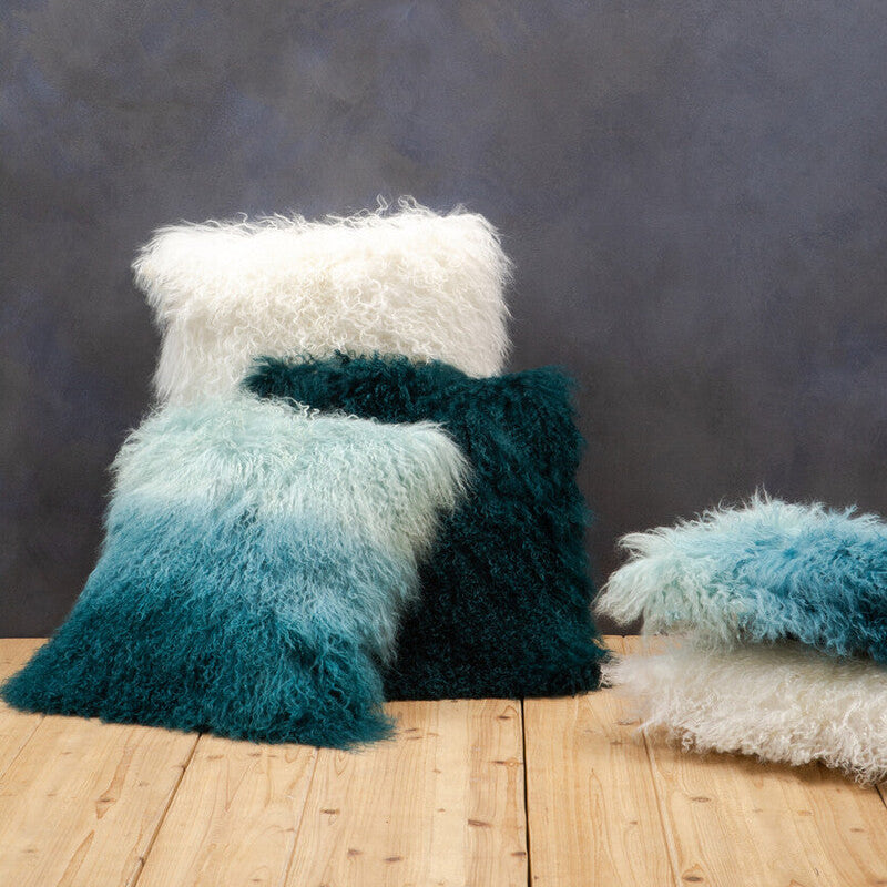 Set of fluffy pillows in white, teal, and blue on a wooden surface with a dark textured wall background.