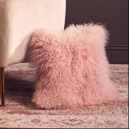 Beige armchair with fluffy white and pink cushions against a dark wall.