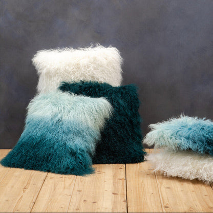 Set of fluffy pillows in teal, white, and blue on a wooden surface with a dark textured background.